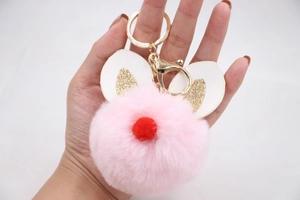 Detailed close-up of pink pompom keychain with bunny ears and golden glitter accents