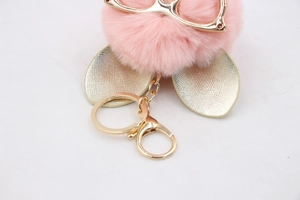 Détail d'un porte-clés pompon rose avec lunettes dorées et mousqueton métallique chic