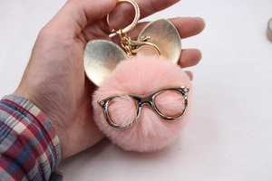 Détail d'un porte-clés pompon rose avec des lunettes dorées et des oreilles de lapin
