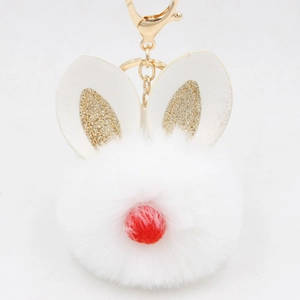 Detail of white fluffy rabbit fur pompom keychain with golden glitter ears and red nose