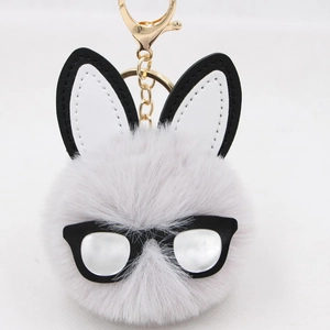 Plush grey rabbit head keychain with black glasses and gold ring on white texture