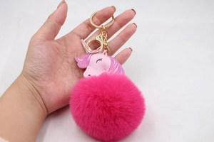 Detail of rose red faux fur pompom keychain with golden unicorn metal hardware