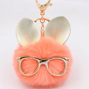 Détail d'un porte-clés pompon en fausse fourrure rose orangé avec lunettes dorées et oreilles