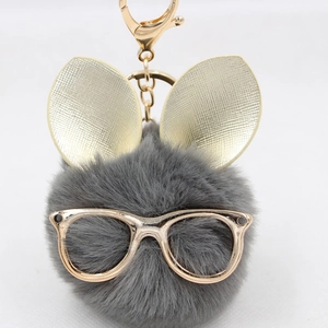 Détail d'un porte-clés pompon gris avec des oreilles de lapin dorées et lunettes