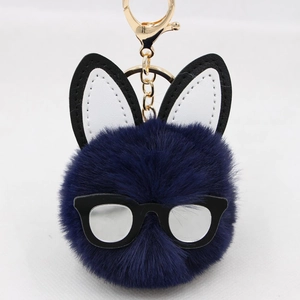 Detail of navy blue faux fur pompom keychain with rabbit ears and black glasses frame