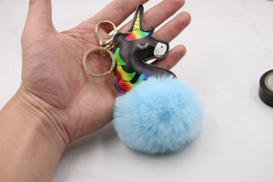 Close-up of black unicorn keychain with a large fluffy light blue pompom and gold clip