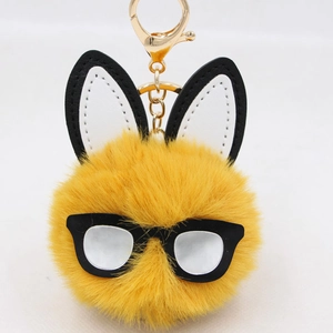 Detailed shot of yellow plush rabbit pompom keychain with round glasses and golden clip