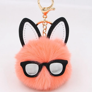 Close-up of pink fluffy rabbit ball keychain with black glasses and golden hardware