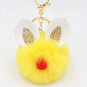 Close-up of yellow faux fur ball keychain with white leather ears and gold glitter