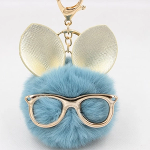 Détail du porte-clés pompon bleu ciel avec oreilles de lapin dorées et lunettes chic
