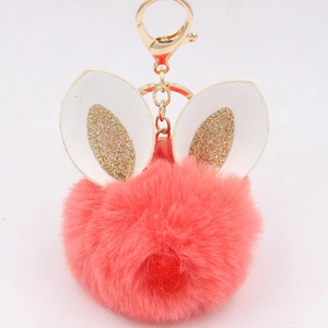 Detail of a fluffy orange-pink faux fur keychain with gold glitter rabbit ears and metal clasp