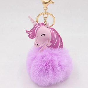 Close-up of pink unicorn head with purple faux fur pompom and golden metal keychain
