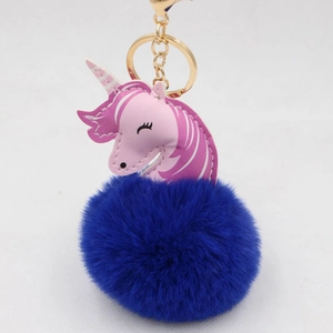 Close-up of deep blue fur pompom unicorn keychain with gold metal clasp and leather head