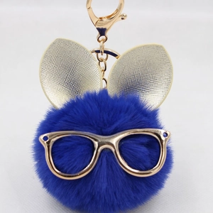 Détail de porte-clés pompon en fausse fourrure bleue avec oreilles de lapin dorées et fermoir