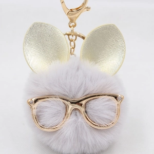 Détail d'un porte-clés pompon gris avec oreilles de lapin dorées et lunettes