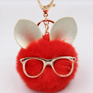 Détail d'un porte-clés pompon rouge avec oreilles de lapin dorées et lunettes chic