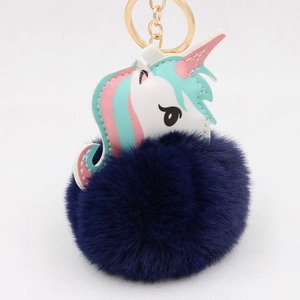 Close-up of a blue fluffy pom-pom unicorn keychain with a golden metal ring and clip
