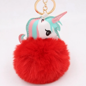 Detail of red faux fur pompom and white leather unicorn head on a gold keychain