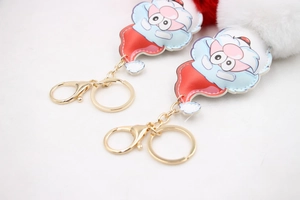 Close-up of two Santa Claus keychains with fluffy faux fur pom poms and golden metal clasps