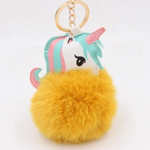 Detail of cute unicorn keychain with soft yellow pom-pom and golden metal ring