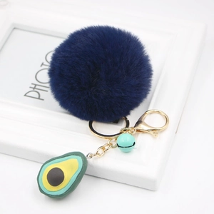 Close-up of navy blue plush ball keychain with a silicone avocado charm and blue bell