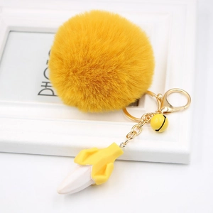 Detail of yellow fluffy pom pom keychain with small banana charm and golden metal clasp