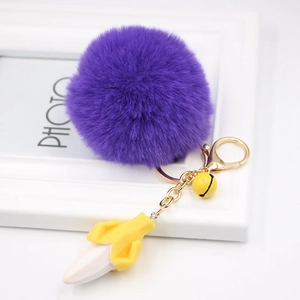 Detail of purple faux fur pompom keychain with golden bell and resin banana pendant