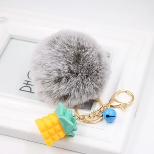 Detail of grey fluffy pompom keychain with golden pineapple charm and blue bell
