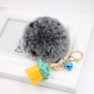 Detail of grey plush pompom keychain with golden pineapple charm and small blue bell