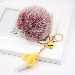 Detail of pink faux fur pompom banana keychain with a yellow bell and gold lobster clasp