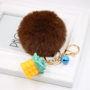 Detail of faux fur pom pom keychain with a yellow silicone pineapple and blue bell charm
