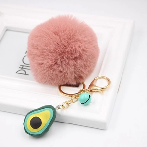 Detail of pink faux fur pompom with avocado pendant and blue bell on gold keychain