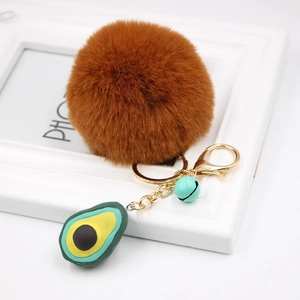 Detail of avocado plush keychain with brown fur ball, gold lobster clasp and green bell