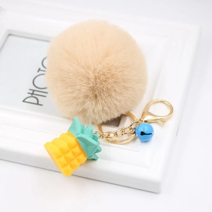 Detail of a beige faux fur pompom keychain with golden pineapple charm and blue bell