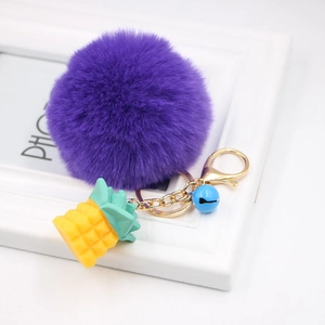 Detail of purple faux fur pompom keychain with golden pineapple charm and blue bell