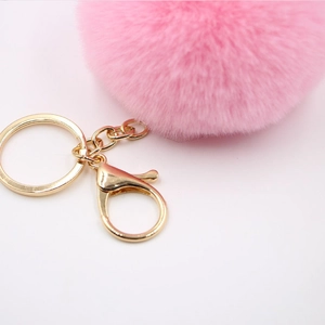 Soft pink faux rabbit fur pom pom keychain with gold metal clasp on white background