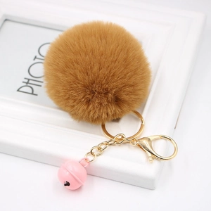 Detailed macro view of a fluffy faux fur pompom keychain with golden metal clasp and pink bell