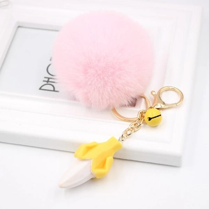 Detail view of pink pompom keychain with a yellow banana charm and golden bell accessory