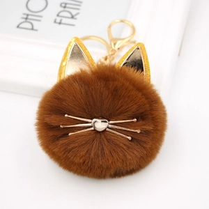 Detailed close-up of brown faux fur cat pom-pom keychain with golden ears and whiskers