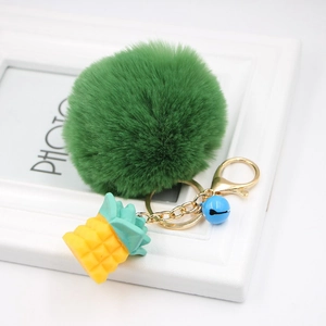 Detail of green faux fur pompom keychain with yellow pineapple charm and blue bell accent