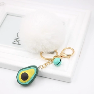 Detail view of avocado charm and white fluffy faux fur pompom on golden keychain