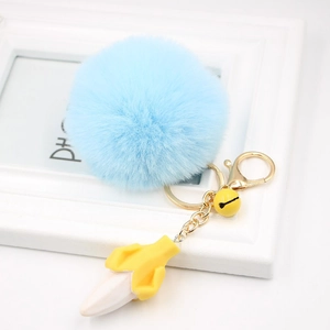 Close-up of fluffy blue pompom keychain with yellow resin banana charm and golden bell