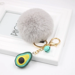 Detail of grey faux fur pompom keychain with a green avocado pendant and golden metal ring
