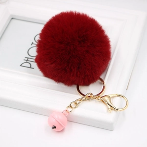 Detail of a deep red faux fur pompom keychain with golden lobster clasp and pink bell charm