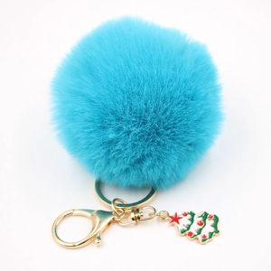 Détail d'un porte-clés pompon bleu sarcelle avec un pendentif sapin de Noël émaillé