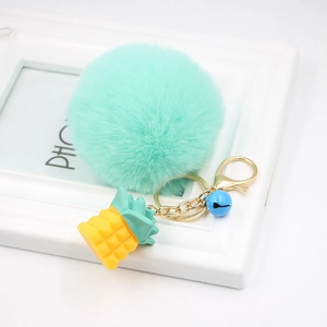 Close-up of mint green pompom keychain with yellow resin pineapple and blue bell