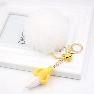 Close-up of fluffy white pompom keychain with a resin banana and gold bell charm