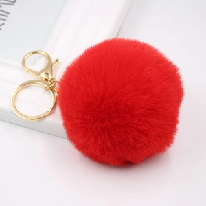 Macro shot of fluffy red faux rabbit fur keychain with golden lobster clasp on white surface