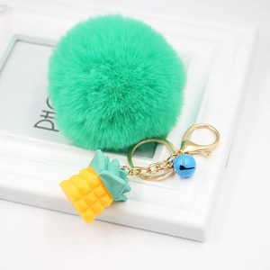 Close-up of mint green faux rabbit fur pompom keychain with golden pineapple charm and blue bell