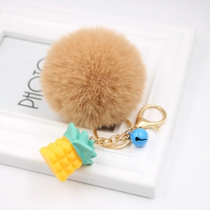 Detail of fluffy khaki faux fur keychain with yellow resin pineapple and blue bell